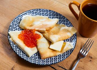 Appetizing baked pancakes served with red caviar and butter on platter