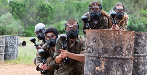 Group of friends paintball players of opposite teams in shootout in forest outdoors