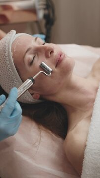 Woman receiving a microcurrent therapy session for facial rejuvenation from a professional cosmetologist at a spa.
