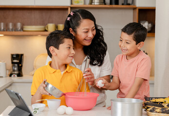 Mom with her Hispanic children preparing a cake at home - family time - happy single mother with...