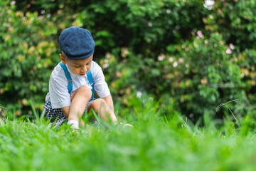 little latino boy sitting on the grass looking down at the ground, wearing a beret and white shirt