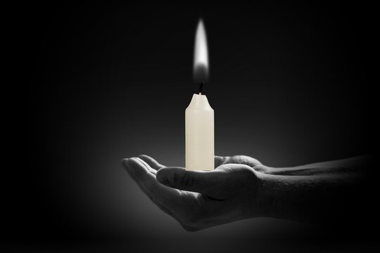 Bright Burning Candle in Human Hands on dark Background.