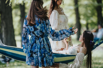 Naklejka premium Two sisters spend quality time in a park, one reclining in a hammock while chatting with the other, highlighting a bond in a serene setting.