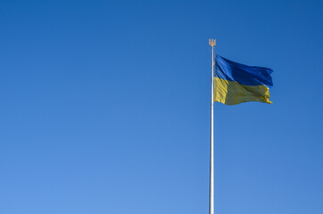 National Ukrainian flag on a flagpole with a trident blowing in the wind against a clear blue sky