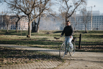 A stylish young adult rides her bicycle on a clear day through a peaceful park, reflecting an...