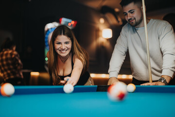 A happy young woman plays pool while a man watches, both enjoying a fun evening together in a bar...
