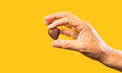 Unrecognizable hand of man isolated on yellow background holding a heart shaped chocolate