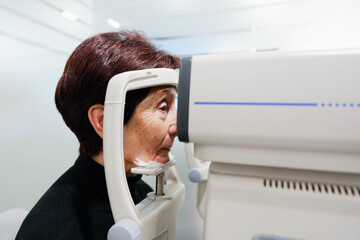Elderly woman using an autorrefractometer in oculist office. Person checking vision.