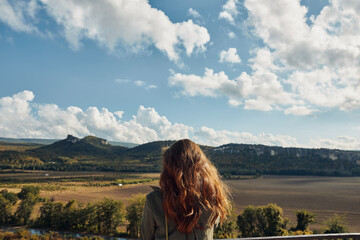 Woman admiring scenic beauty of landscape with blue sky and clouds in background during travel...