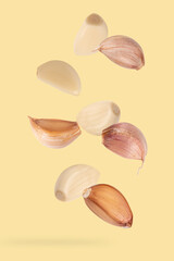 Garlic cloves falling on yellow background.