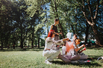 A group of friends seated on grass in a park, sharing pink cotton candy on a cheerful, sunny day, surrounded by trees and enjoying each other's company.