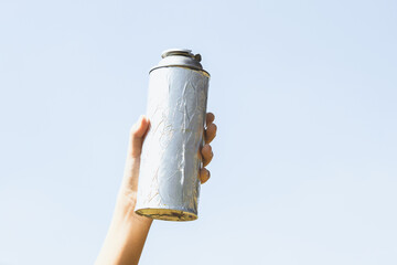 Recyclable can waste held in hand up on sky-like isolated background. Hand holding can waste for...