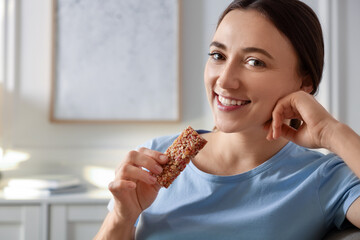 Woman holding tasty granola bar at home