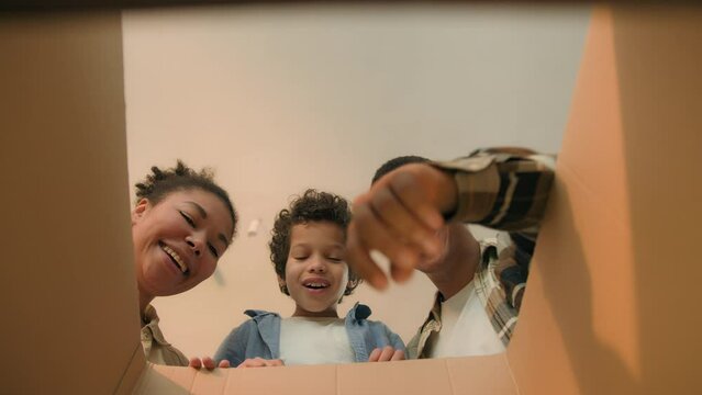 Point of view POV open box African american family parents son unpacking cardboard parcel happy funny little boy child kid surprise teddy bear toy birthday present moving day online shopping delivery