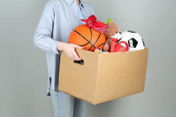 Woman holding box of unwanted stuff on grey background, closeup - Powered by Adobe