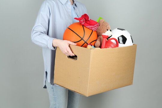 Woman holding box of unwanted stuff on grey background, closeup