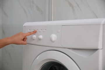 Woman pressing button on washing machine in bathroom, closeup