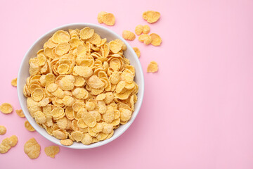 Breakfast cereal. Tasty corn flakes in bowl on pink table, top view. Space for text