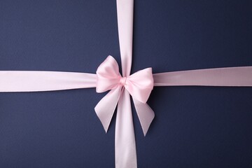 Pink satin ribbon with bow on blue background, top view