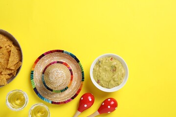 Mexican sombrero hat, tequila, nachos chips, guacamole and maracas on yellow background, flat lay....