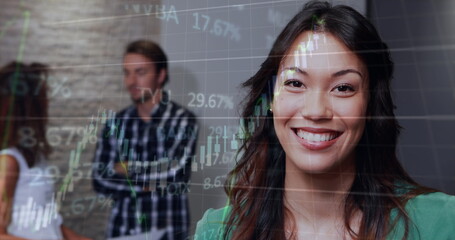 Image of graphs and trading board, biracial smiling businesswoman with coworkers in background