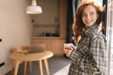 Portrait of happy cheerful young woman holding cup enjoy smell coffee or tea and drinking with...