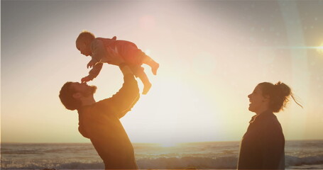 Image of glowing spots over caucasian parents with baby by the sea