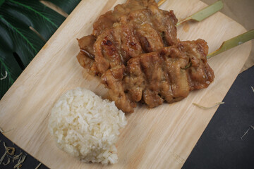 Sticky rice with grilled pork on wooden cutting board. Moo ping is grilled pork in traditional Thai...