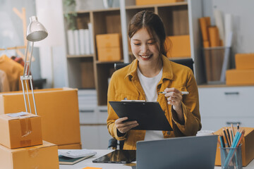 Asian SME business women use laptop computer checking customer order online shipping boxes at home....