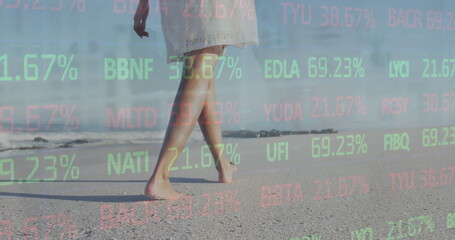 Image of trading board over low section of african american woman walking on beach - Powered by Adobe