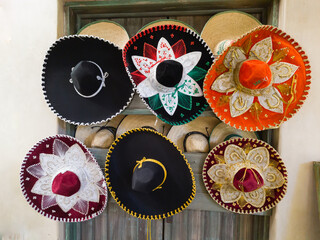 Six Mexican charros hats of several colors hanging on a wall