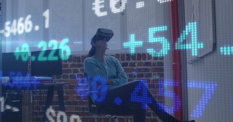 Image of trading board over caucasian woman sitting on chair and using vr headset in office