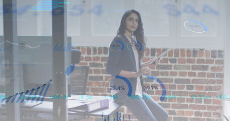 Image of multiple graphs and trading board over caucasian woman using digital tablet in office