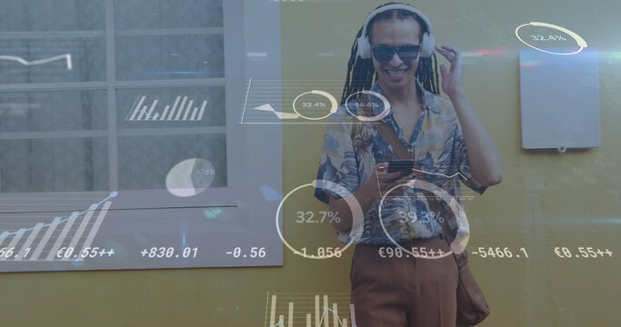 Image of graphs, trading board, biracial man with headphones listening to music on cellphone - Powered by Adobe
