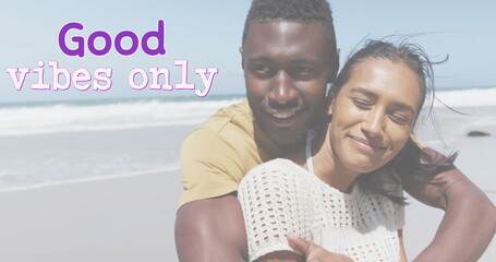 Fototapeta premium Image of the words good vibes only in purple over happy couple embracing on beach