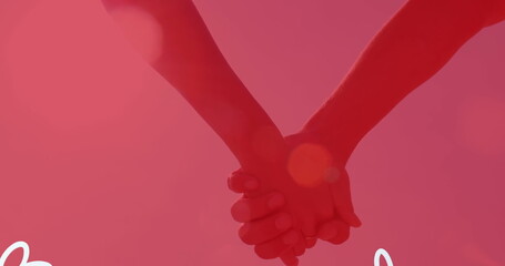 Two people holding hands against pink background