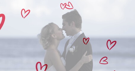 Caucasian couple wearing wedding attire, kissing on beach