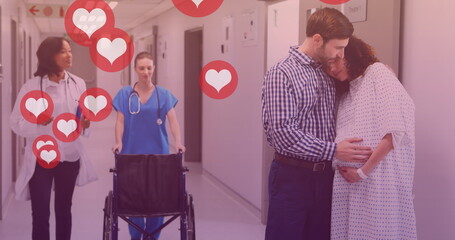 Image of heart icons over caucasian man embracing pregnant wife in hospital
