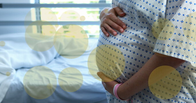 Image of green spots over biracial pregnant woman touching her stomach in hospital