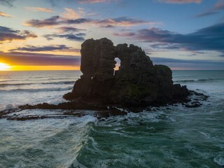 Waves crashing over Rocky island with keyhole in it and wild surf at sunset in Anawhata on the west coast of Auckland, New Zealand.