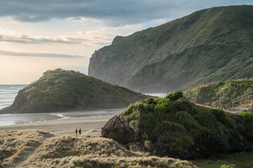 Two people walking over tussock grass and sandunes on Anawhata beach, west coast of Auckland, New...