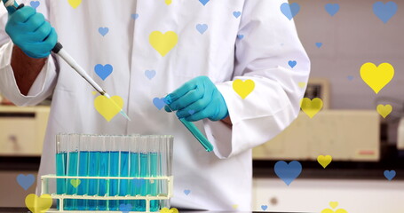 Image of yellow and blue hearts falling over midsection of biracial male lab worker