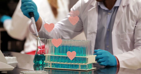 Image of hearts over caucasian male scientist using pipette in lab