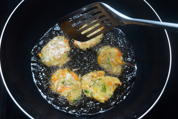 Someone is turning a dough of raw vegetables and wheat flour which is fried