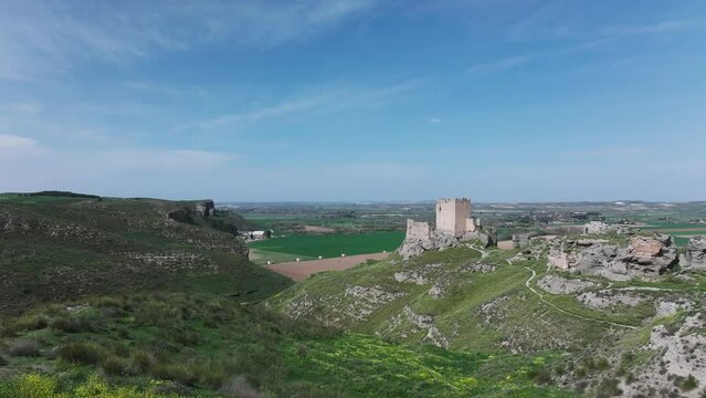 drone flight taking off from a platform viewing the 9th century Oreja castle and the remains of its walls behind in an intense green there are crop fields with a blue sky in Ontigola Toledo Spain