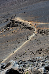 Looking down into the Haleakalā volcano crater at people on horseback going down the trail cut into the lava rock, high altitude dry arid trail ride expedition, Haleakalā National Park, Maui, Hawaii
