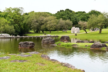 A picturesque park featuring rich natural landscapes and cultural elements, highlighted by stones, ponds, and tree-shaded pathways for leisurely strolls.