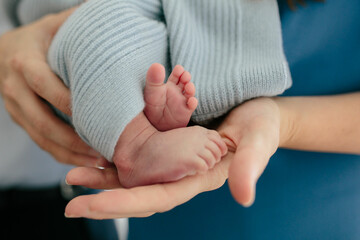 hands of woman in blue dress holding tiny newborn feet sticking out of blue knit blanket