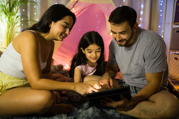 Family shares a cozy and intimate evening inside a tent with fairy lights using a tablet for movies and games