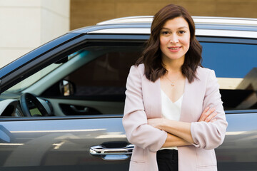 Professional woman in a smart business attire standing confidently beside her car, portraying...
